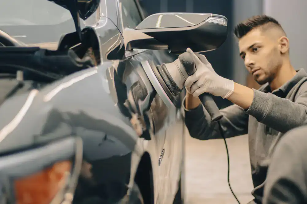 Technician operating a dual action polisher on a vehicle panel